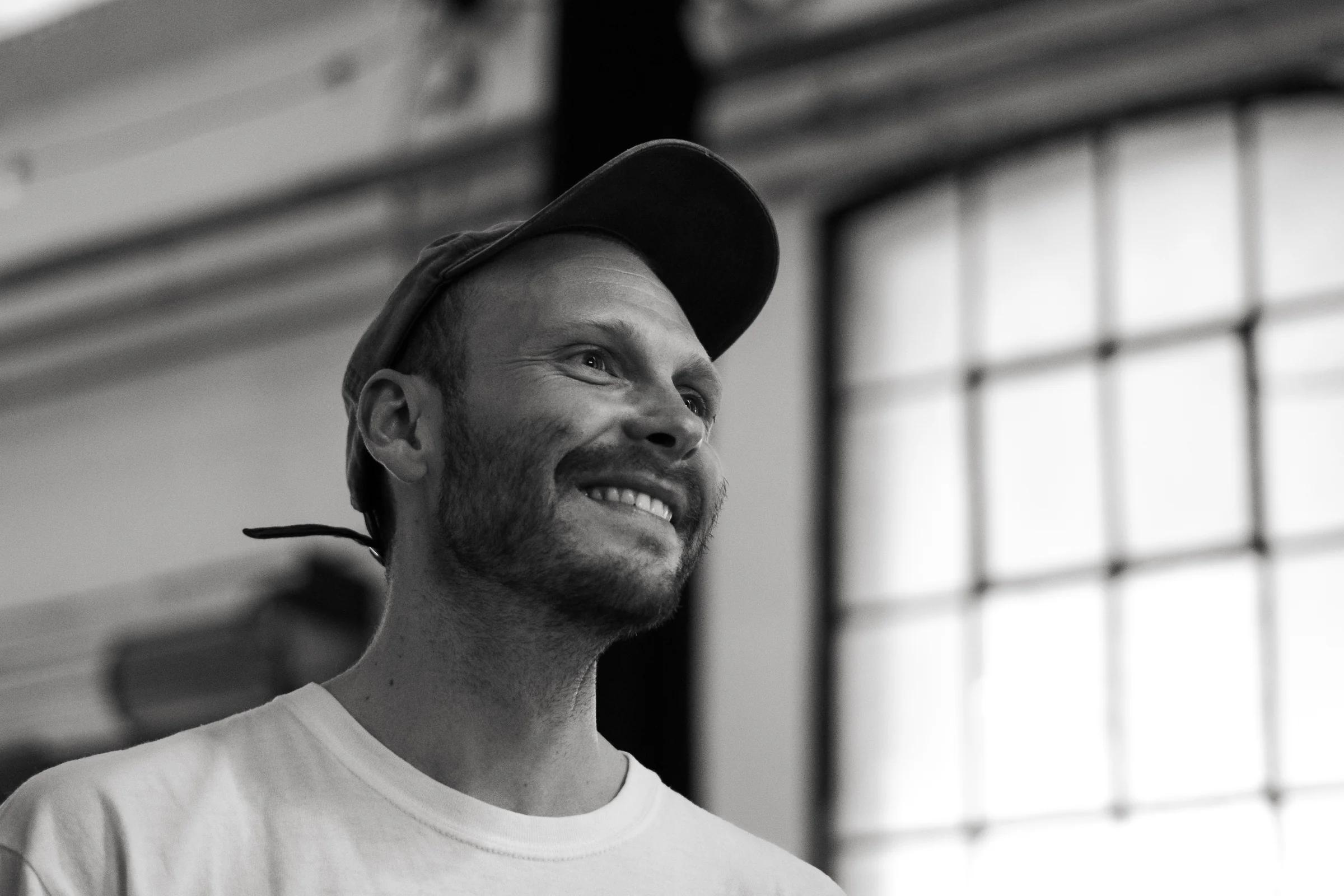 Black and white portrait of a practitioner, cap on, window light behind.