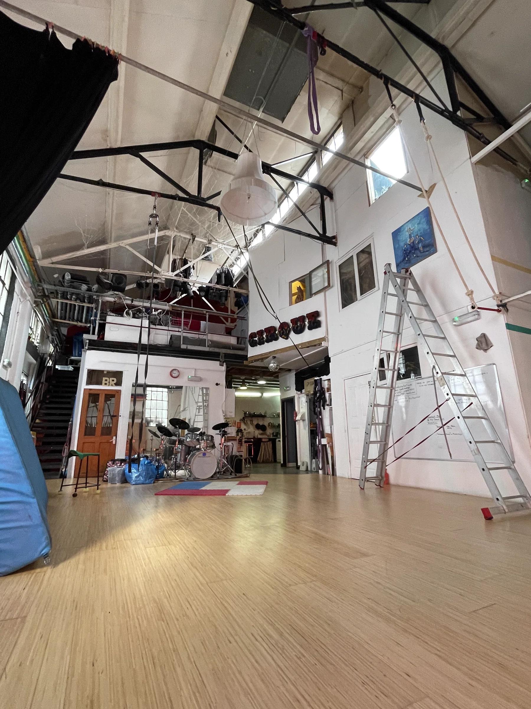 Wide view of the interior — high steel trusses, drum kit, white painted brick.